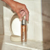 Hand holding a bottle of Galactin skincare product on a bathroom shelf.
