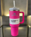 Pink Stanley Quencher H2.0 FlowState tumbler with straw, handle, and lid on reflective surface, insulated stainless steel travel cup.