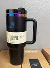 Stanley 40 oz Quencher H2.0 tumbler in black iridescent chrome with colorful accents on a wooden surface, vacuum insulated and spill-resistant