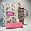 Stanley x LoveShackFancy 40oz floral design holiday tumbler with pink handle next to a matching pink towel on gray background
